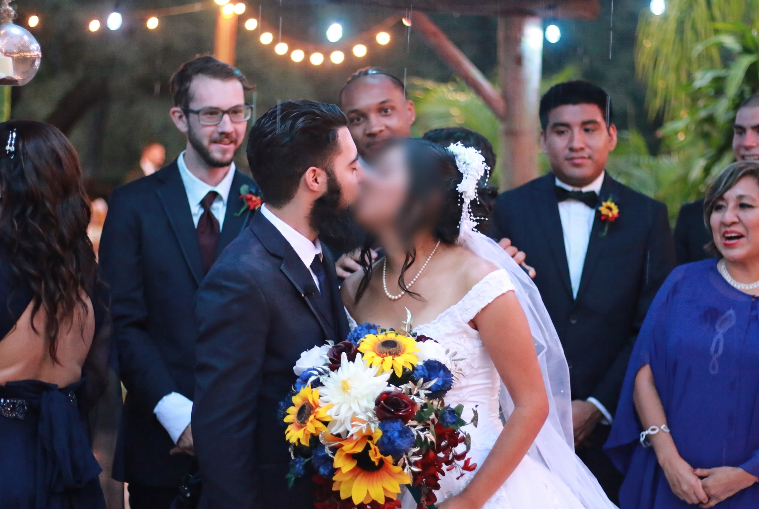 Elias and Nada kissing at their wedding ceremony beneath string lights